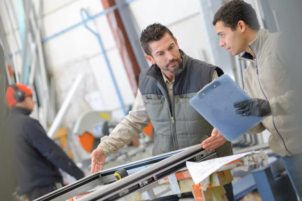 employés d’une usine de menuiserie en train de vérifier les dimensions d’une fenêtre sur-mesure